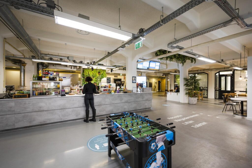 Modern café area on Van Diemenstraat with a customer at the counter and a foosball table in the foreground.